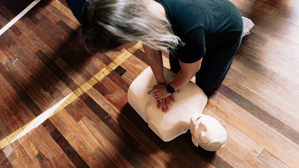 A person practices CPR on a training mannequin indoors.